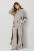 Woman wearing a beige long-sleeve shirt and wide-leg pants against a white background