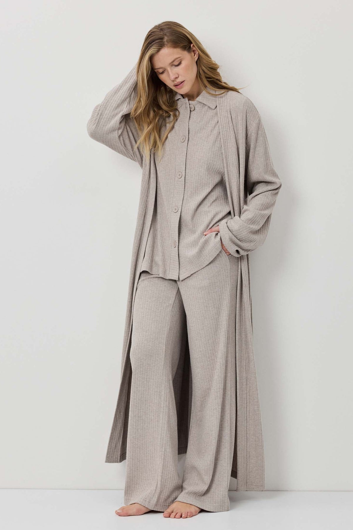 Woman wearing a beige long-sleeve shirt and wide-leg pants against a white background
