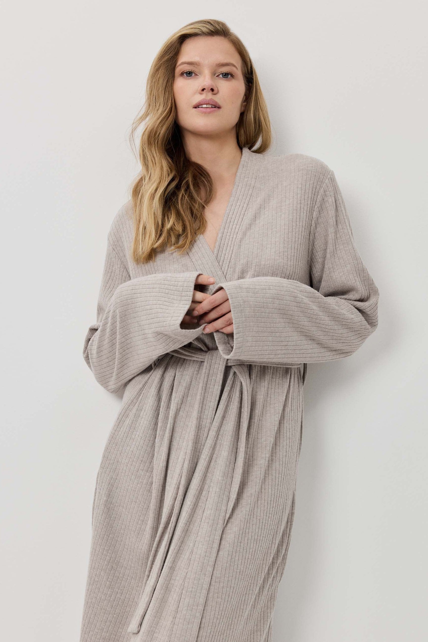 Woman wearing a long beige ribbed robe against a white background