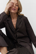 Woman wearing a black pinstripe pajama set against a white background