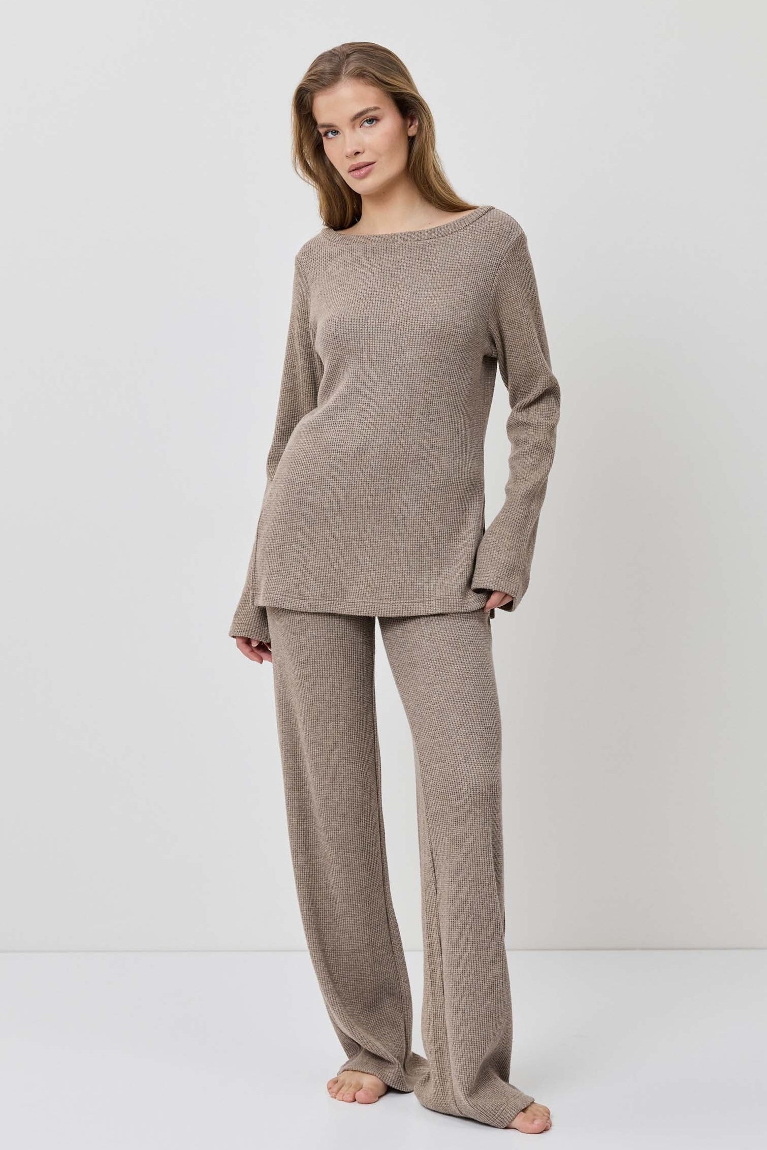 Woman wearing a beige long-sleeve top and pants on a white background