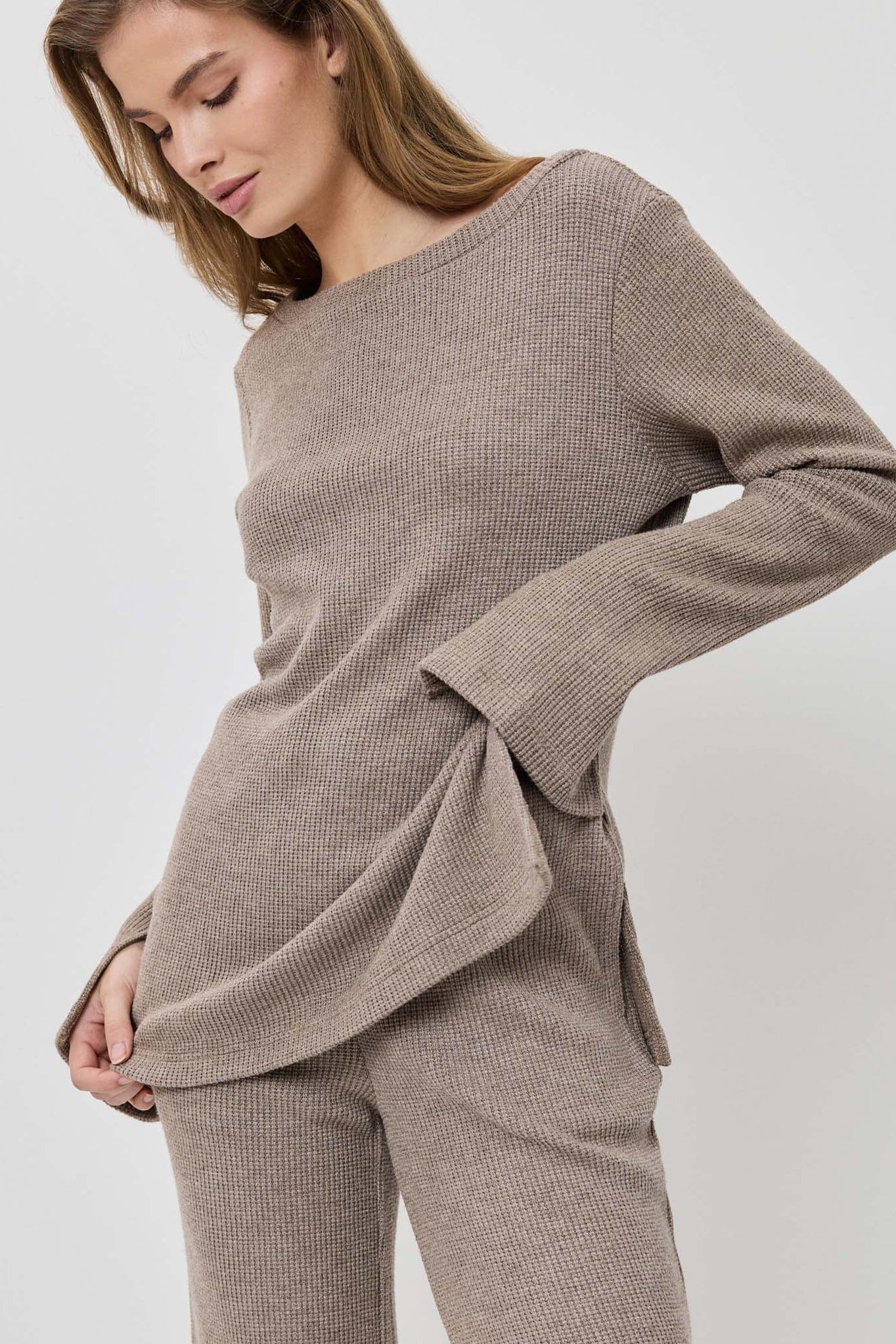 Woman wearing a beige sweater and pants on a white background