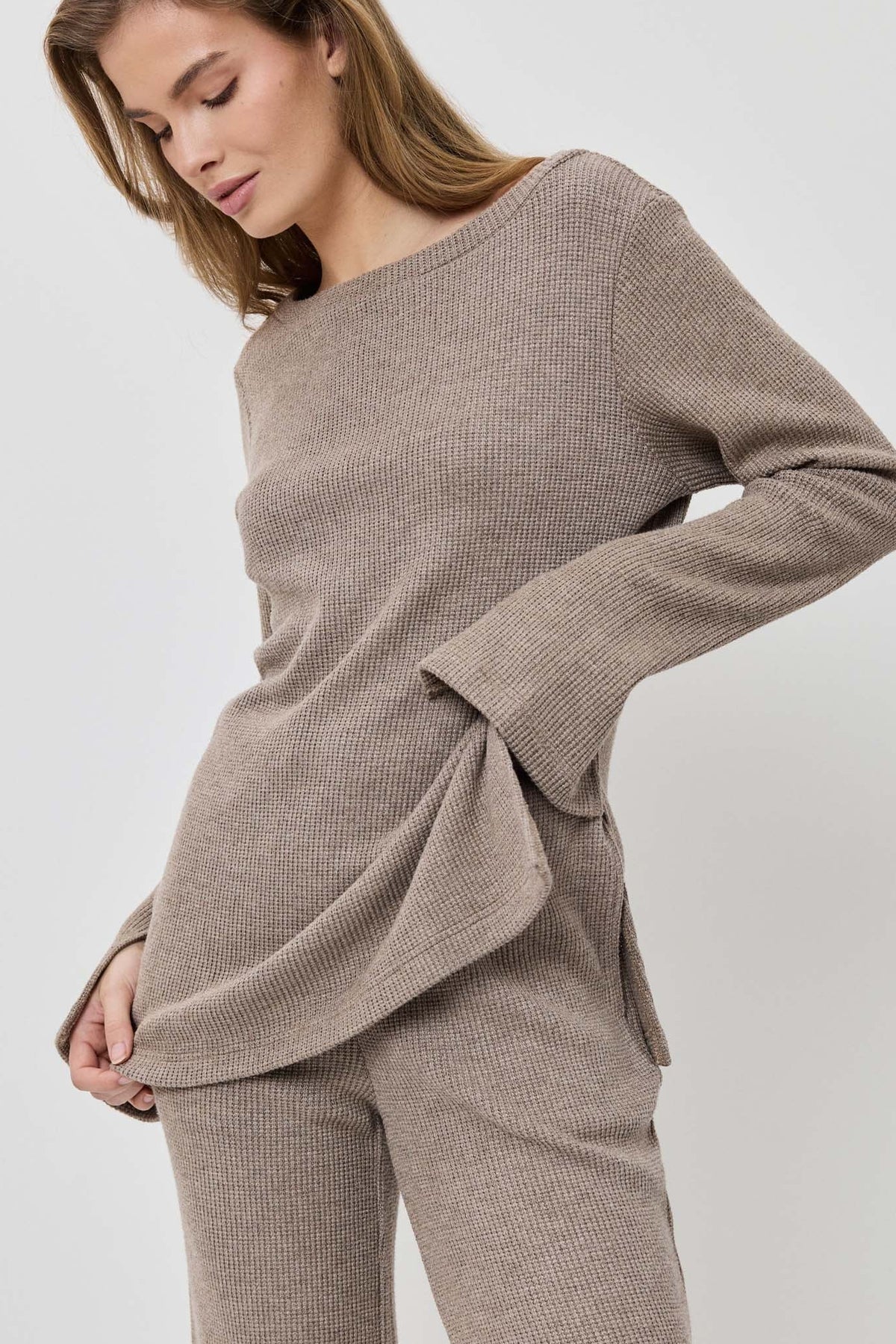 Woman wearing a beige sweater and pants on a white background