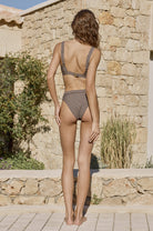 Woman in a bikini standing in front of a stone wall and building.