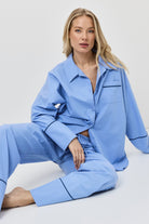 Woman wearing a light blue pajama set sitting on a white surface with a white background