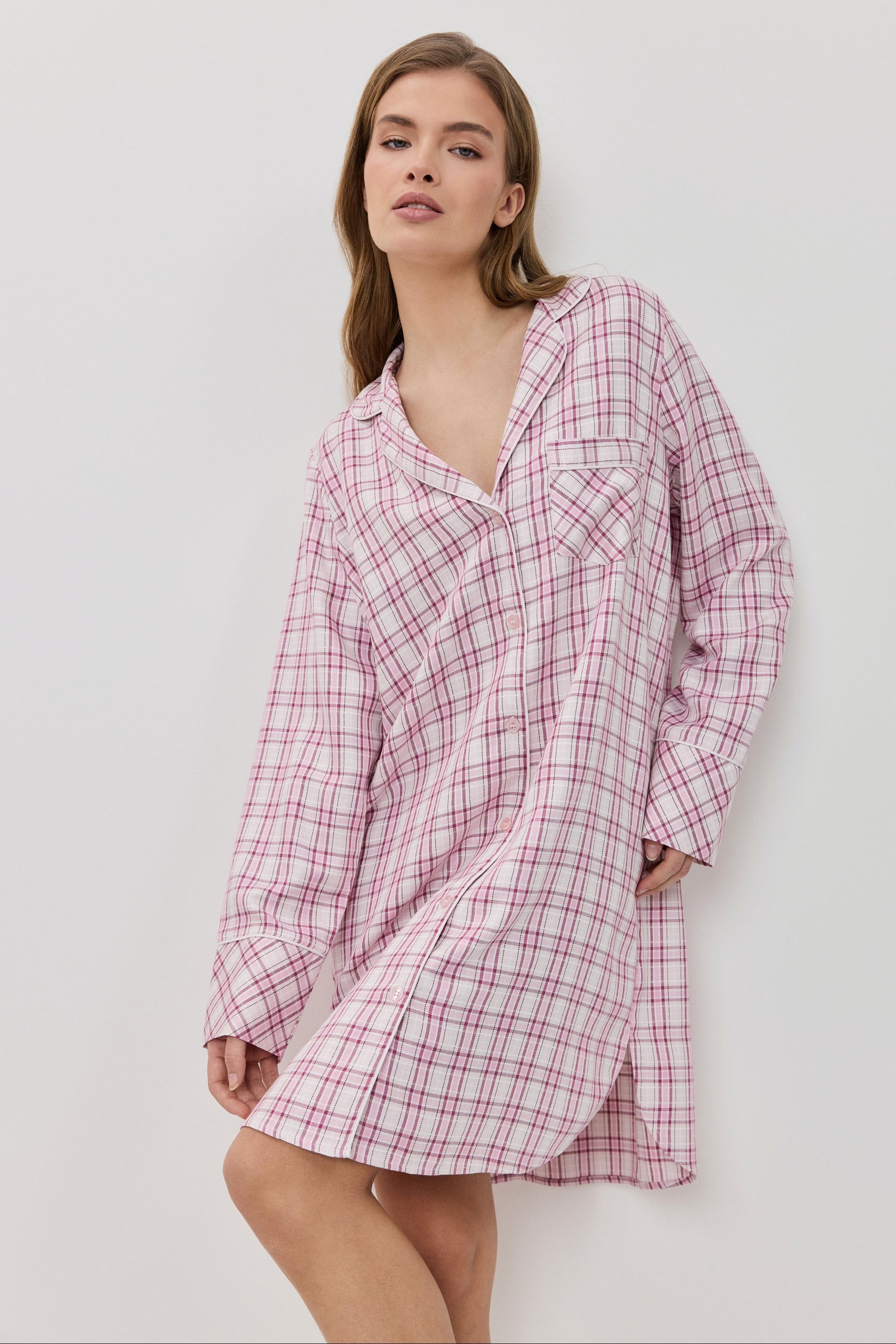 Woman wearing a pink plaid nightshirt against a white background