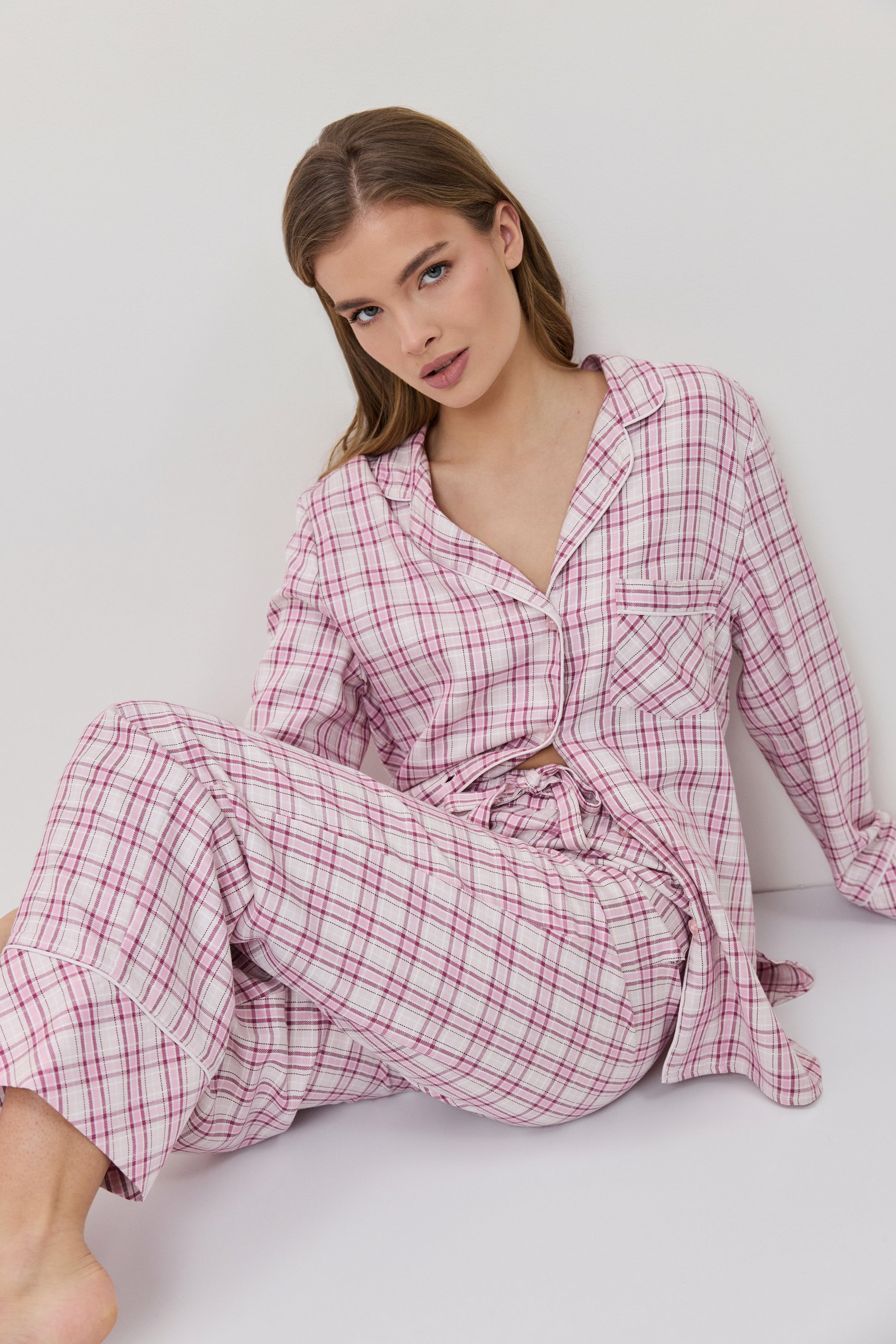 Woman wearing a pink plaid robe sitting on a white surface.