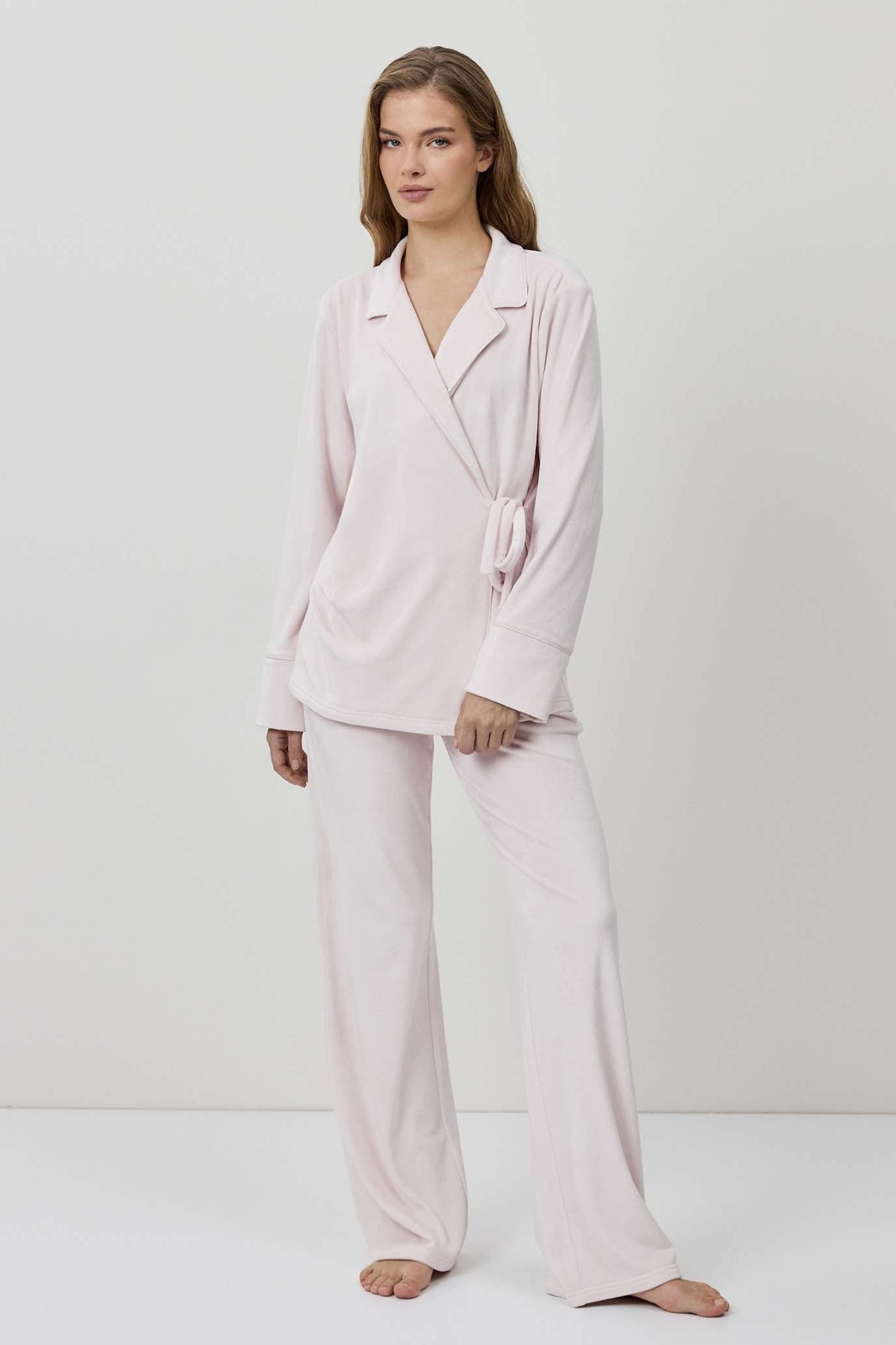 Woman wearing a light pink pajama set against a white background