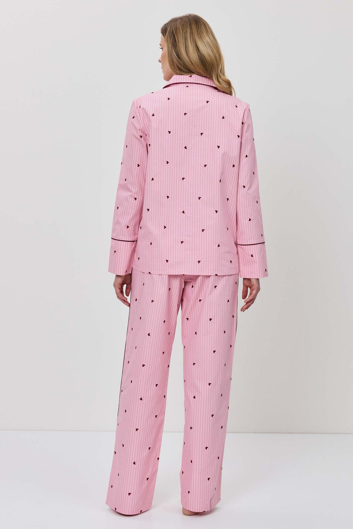 Person wearing a pink pajama set with hearts on a white background