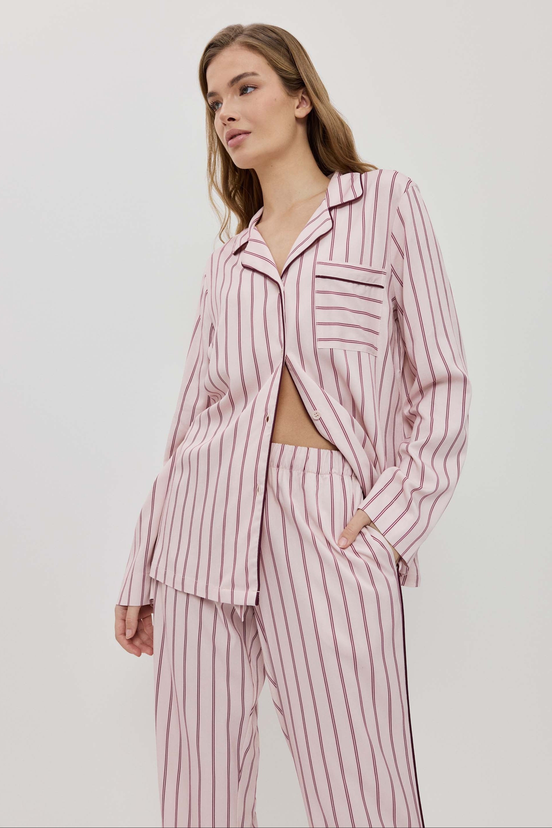 Woman wearing a pink and white striped pajama set on a light gray background