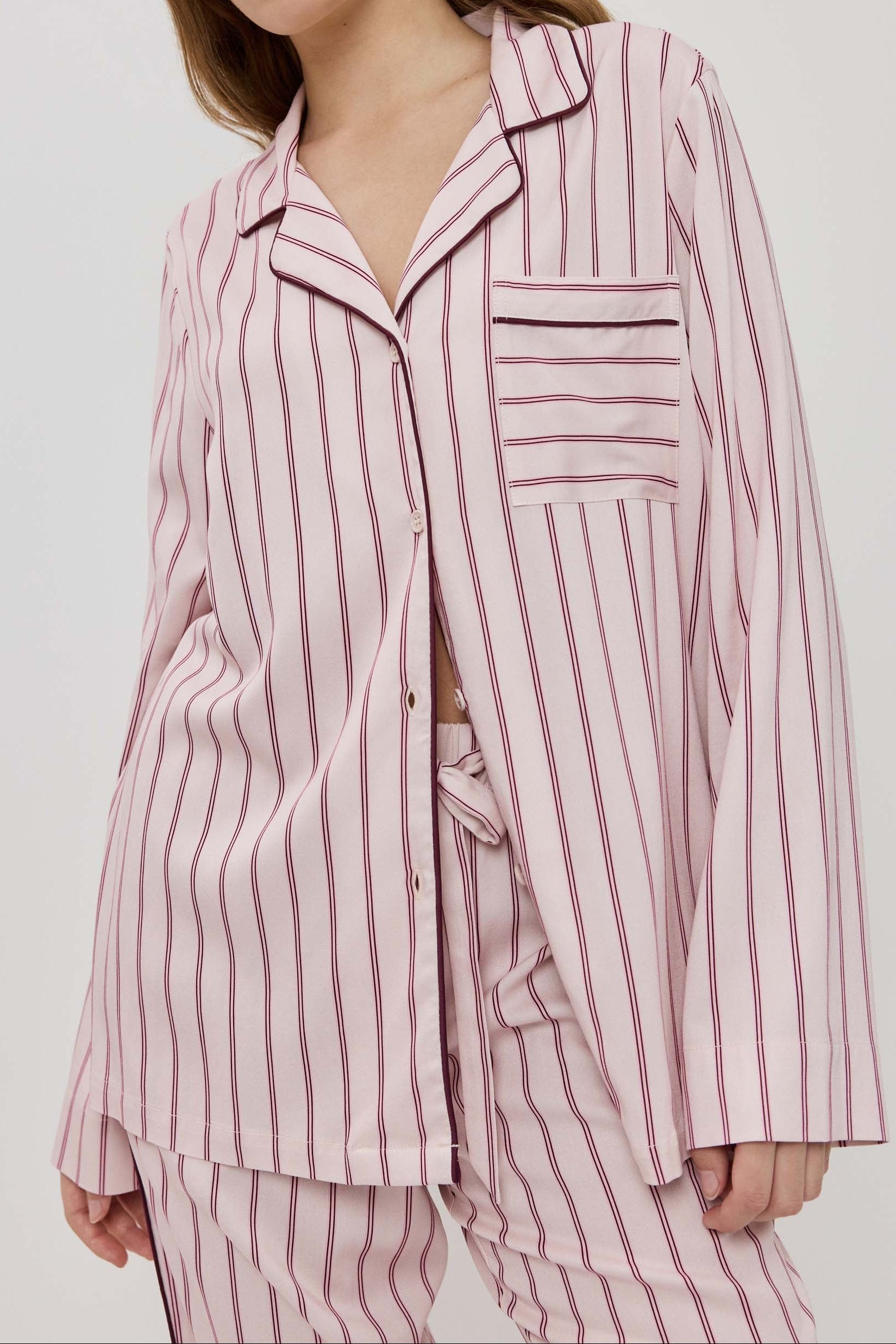 Woman wearing a pink striped pajama set against a white background