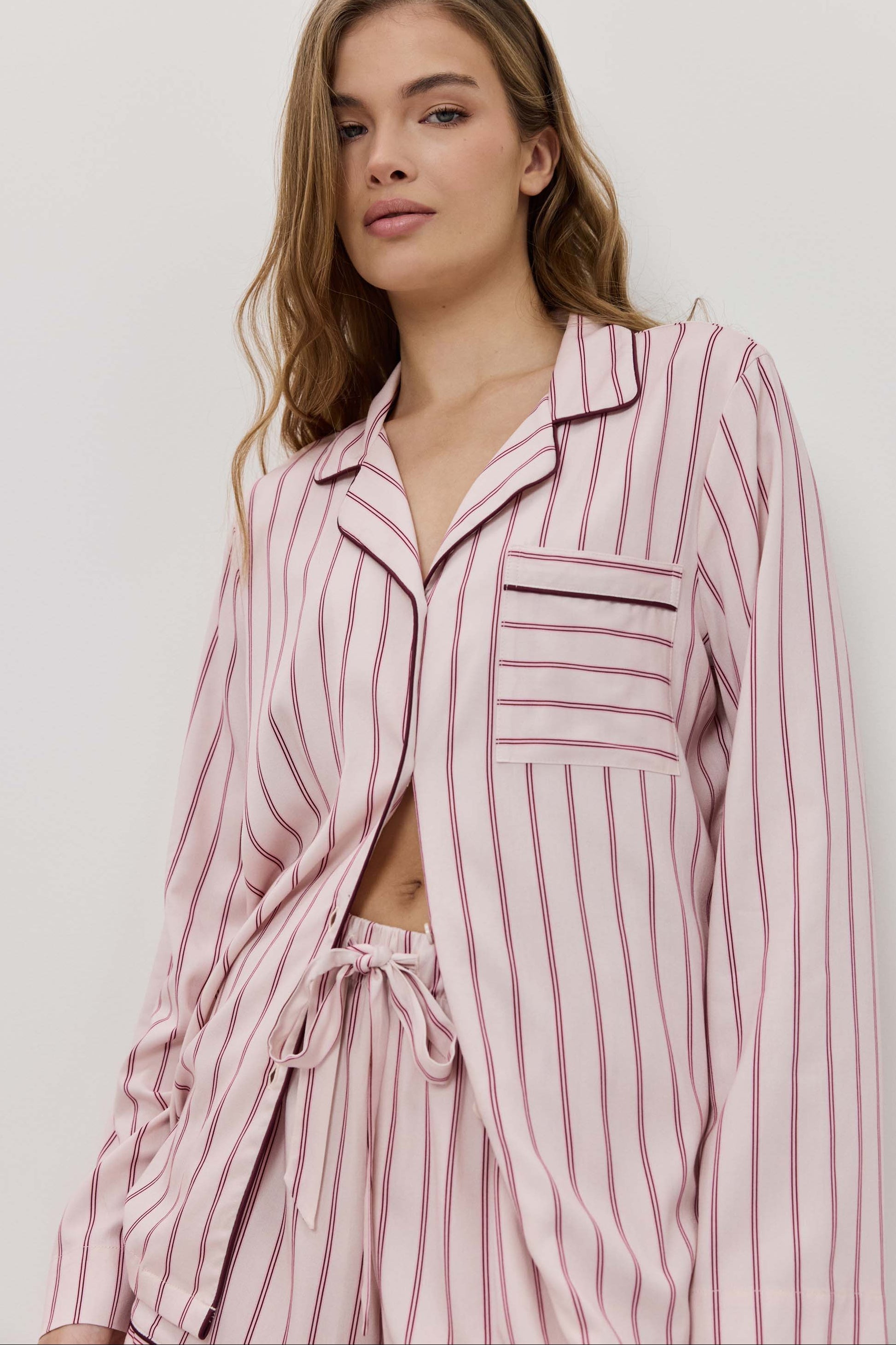 Woman wearing a pink striped pajama set against a plain background