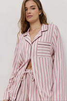 Woman wearing a pink striped pajama set against a plain background