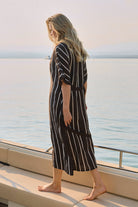 Woman in a striped dress standing on a boat deck with a scenic ocean view.