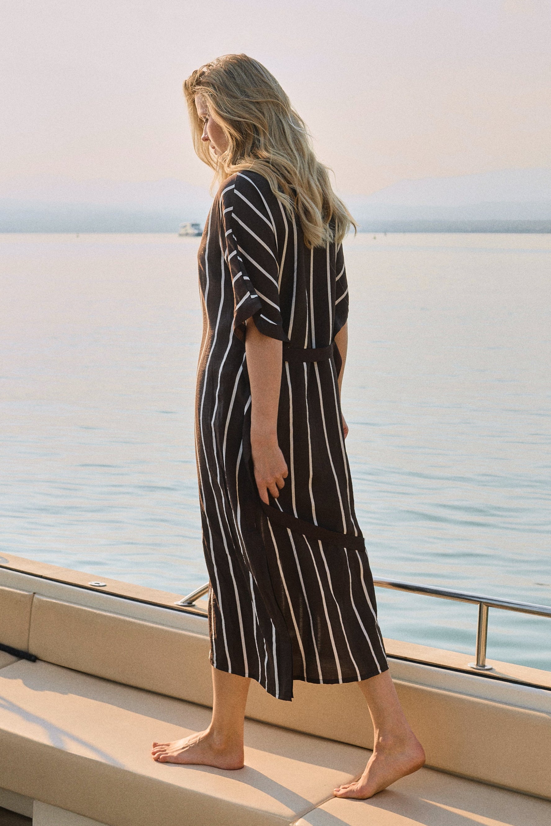 Woman in a striped dress standing on a boat deck with a scenic ocean view.