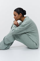 Woman wearing a light green outfit sitting on a white background