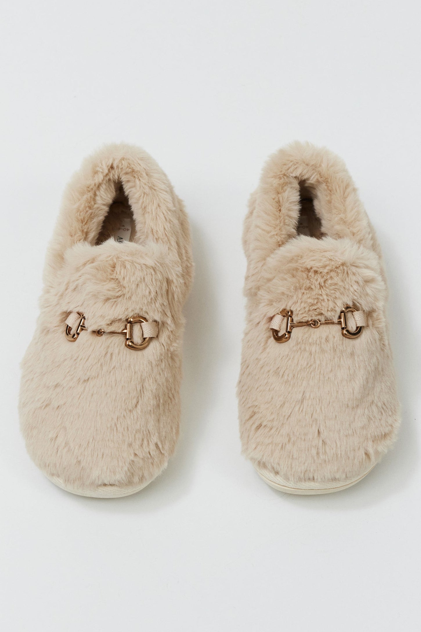 Pair of beige slippers with decorative buckles on a light gray background