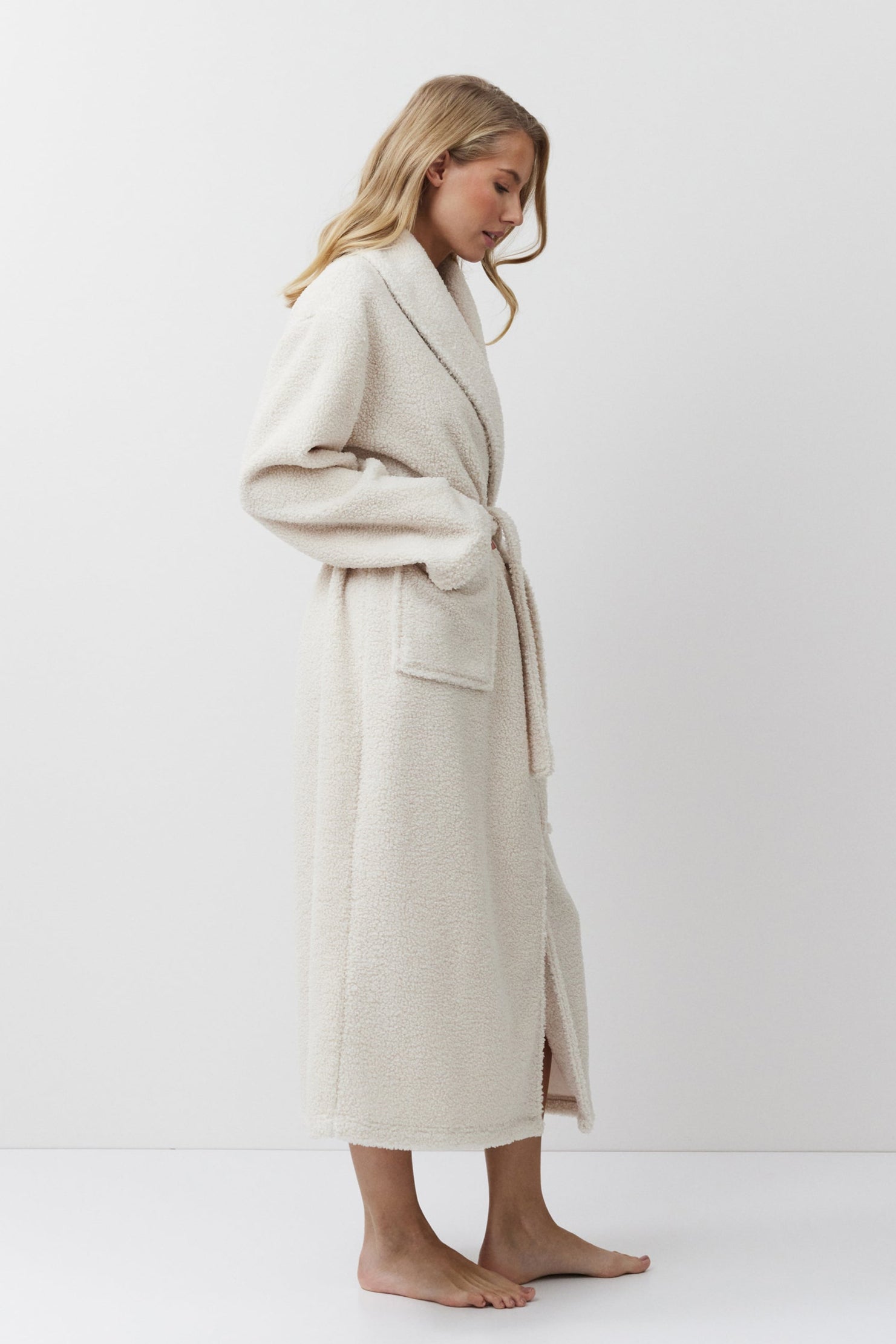 Woman wearing a long beige bathrobe on a white background