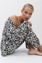 Woman wearing a black and white patterned pajama set sitting on a white background
