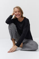 Woman wearing a black long-sleeve top and black and white striped pants sitting on a white floor.