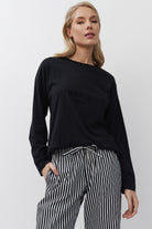 Woman wearing a black sweatshirt with 'Paris' text and striped pants on a white background