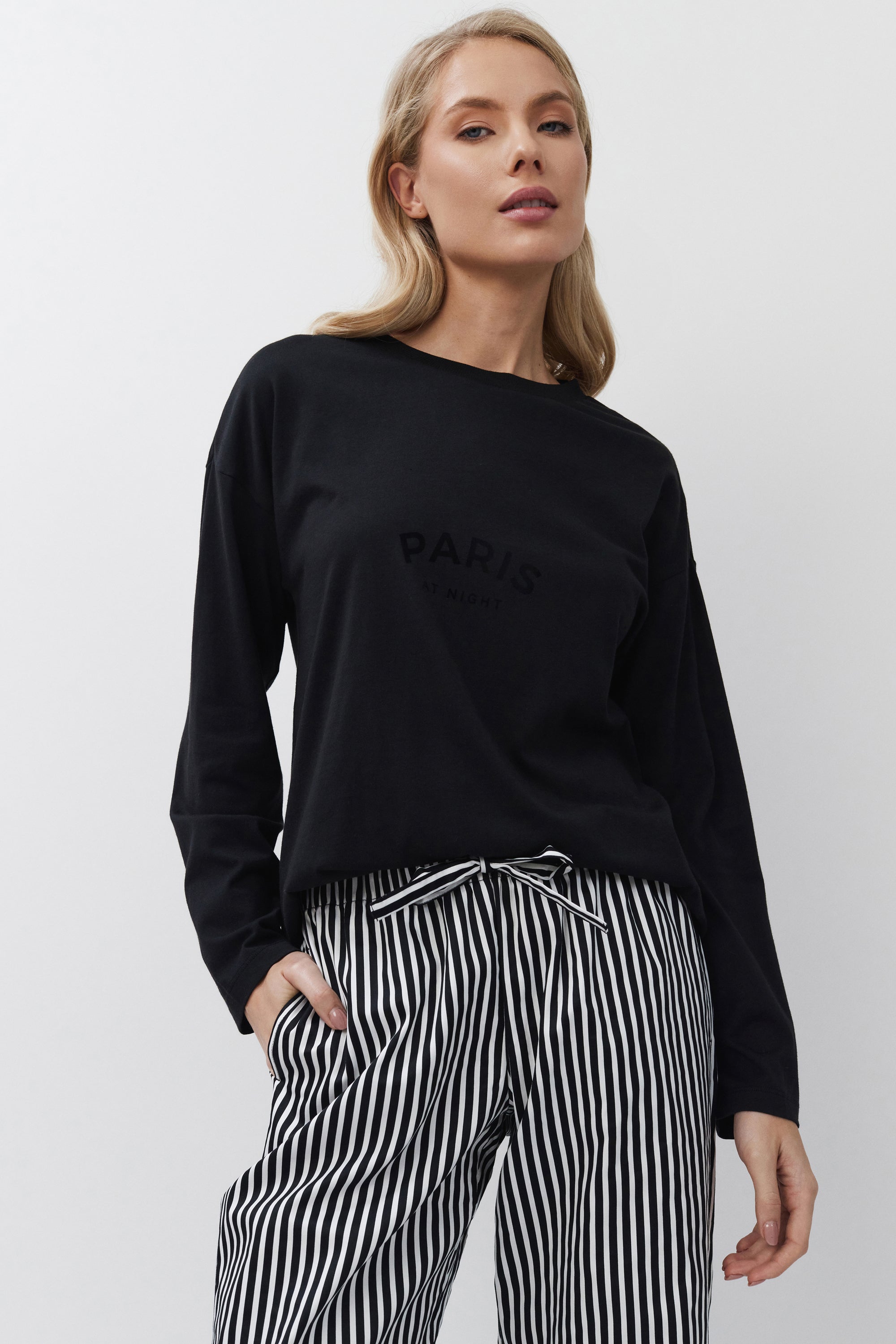Woman wearing a black sweatshirt with 'Paris' text and striped pants on a white background