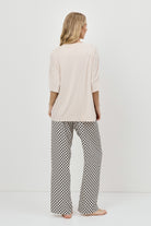 Woman wearing a beige top and patterned pajama pants on a white background