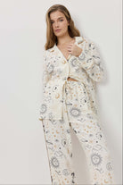 Woman wearing a white pajama set with celestial pattern on a plain background